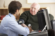 Doctor taking senior man's blood pressure at home