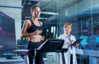 Beautiful Woman Athlete Runs on a Treadmill with Electrodes Attached to Her Body, Female Physician Uses Tablet Computer and Controls EKG Data Showing on Laboratory Monitors.